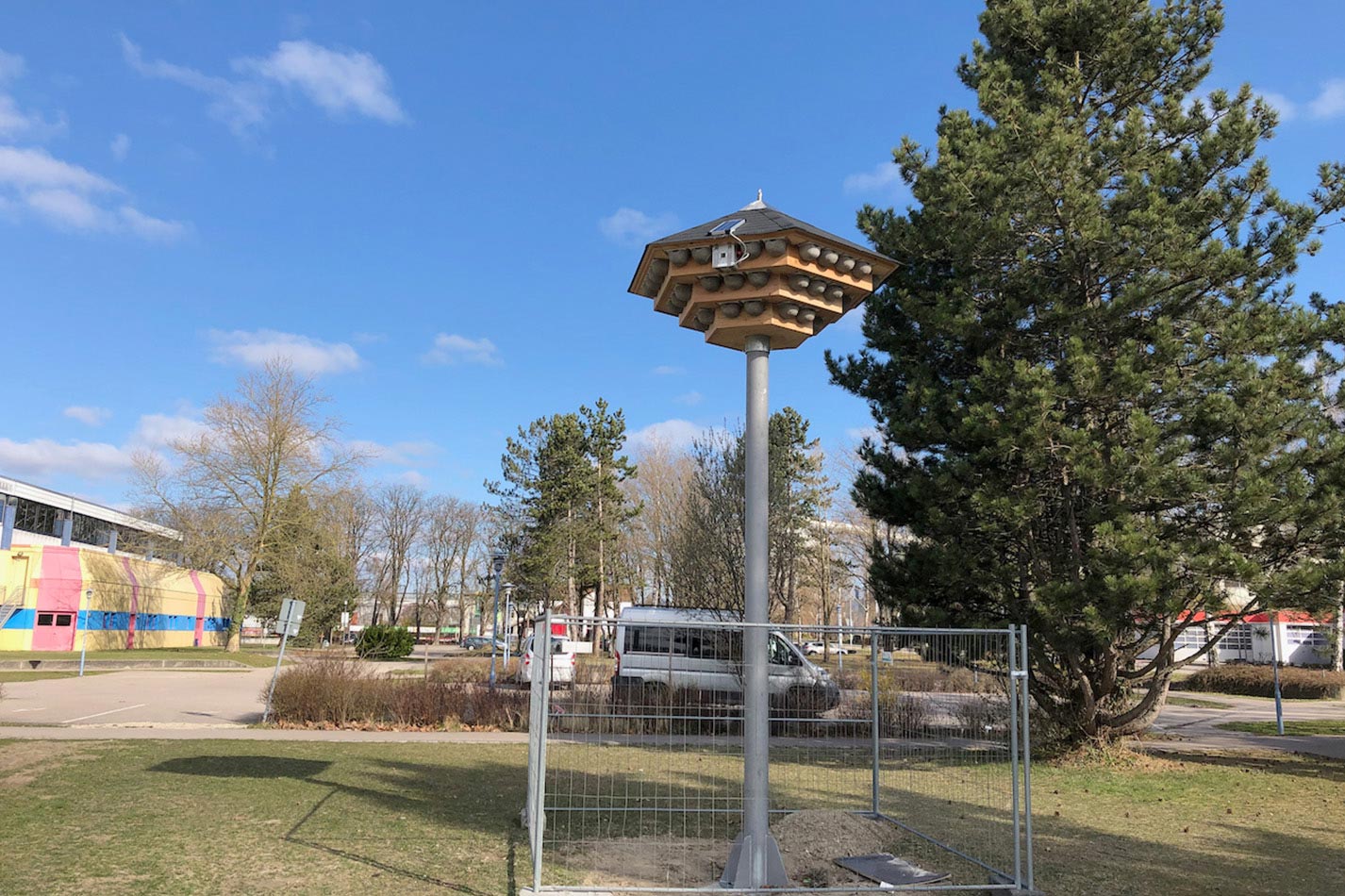 Ein dreistöckiges Schwalbenhaus aus Holz mit Kunstnestern für Mehlschwalben auf einem Stahlmast mit einer Klangattrappe auf einer Wiese